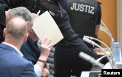 Seorang terdakwa yang diborgol menutupi wajahnya setibanya di ruang sidang di Stuttgart, Jerman, 29 April 2024. (Bernd Weißbrod/Pool via REUTERS)