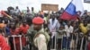 A Nigerien police officer stand guard outside the Niger and French airbases in Niamey as supporters of Niger's National Council for the Safeguard of the Homeland (CNSP), holding a sign and Russian flag, rally, Aug. 27, 2023.