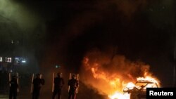 Polisi antihuru-hara berhadapan dengan para demonstran di dekat mobil yang terbakar dalam kerusuhan yang terjadi di Dublin, Irlandia, pada 23 November 2023. (Foto: Reuters/Clodagh Kilcoyne)