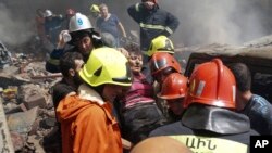 Para petugas pemadam kebakaran mengevakuasi seorang perempuan yang terluka dari lokasi kebakaran akibat ledakan di gudang penyimpanan kembang api di Pasar Surmalu di Yerevan, Armenia, pada 14 Agustus 2022. (Foto: AP/Daniel Bolshakov)