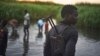 FILE - An unidentified man with a gun stands watch over displaced people, who have taken shelter from fighting, in a rebel-held part of Leer county, in Unity State, South Sudan.