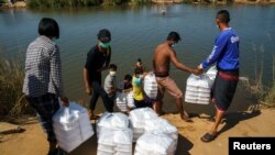 Pengungsi, yang melarikan diri dari gejolak pertempuran antara tentara Myanmar dan kelompok pemberontak dan menetap sementara di Tepi Sungai Moei, menerima bantuan dari Thailand di Mae Sot, Thailand, 7 Januari 2022. ( Foto: REUTERS/Athit Perawongmetha)