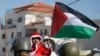 FILE - A Palestinian child dressed as Santa Claus holds a Palestinian flag while standing in front of Israeli Border Police during a demonstration in Al-Masara, near Bethlehem, Dec. 20, 2013 