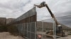 FILE - Workers raise a taller fence along the Mexico-US border between the towns of Anapra, Mexico and Sunland Park, New Mexico, Nov. 10, 2016. For almost two decades, a Mass has been celebrated there on the Day of the Dead to remember migrants who have 