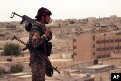 FILE - This April 30, 2017, photo provided by the Syria Democratic Forces (SDF), shows a fighter from the SDF carrying weapons as he looks toward the northern town of Tabqa, Syria.
