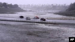 Kendaraan melintasi kolam pengendali banjir yang hampir mencapai jalan, Minggu, 20 Agustus 2023, di Palm Desert, California. (Foto: AP)