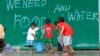 Children help to carry pails of drinking water as they walk past graffiti calling for help after Typhoon Haiyan devastated Tacloban city, central Philippines, Nov. 12, 2013.