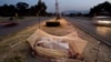 FILE - Vehicles move past Pakistani day laborers sleeping under a mosquito net in the middle of a road in Islamabad, Pakistan.
