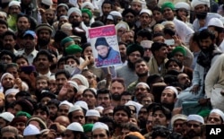 People hold the photo of police officer Mumtaz Qadri, the convicted killer of a former governor, during his funeral, in Rawalpindi, Pakistan, Tuesday, March 1, 2016.