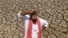 FILE - An Indian farmer looks skyward as he stands on a dried bed of a water body on the outskirts of Ahmadabad, India.