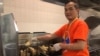 Satriyo Utomo alias Nanang, ketua tim relawan dapur Muktamar IMSA 2019, menggoreng ikan filet di dapur (VOA/Karlina).