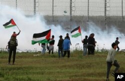 FILE - Protesters wave Palestinian flags amid teargas fired by Israeli troops near a fence on the Gaza Strip border with Israel, east of Gaza City, March 30, 2019.