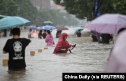 Warga mengarungi banjir di jalan yang banjir di tengah hujan deras di Zhengzhou, Provinsi Henan, China, 20 Juli 2021. (Foto: China Daily via REUTERS)