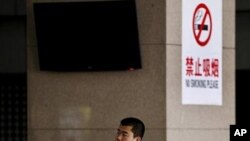 FILE - A Chinese man smokes in front of a pillar with a no smoking notice on display at a bus station in Beijing, March 24, 2011
