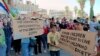 In this photo released by Suwayda24, people hold placards during a protest in the southern city of Sweida, Syria, Aug. 26, 2023. 