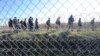 FILE - Migrants walk behind a temporary protective fence at the border between Hungary and Serbia near Morahalom, southeast of Budapest, Hungary, Feb. 22, 2016.