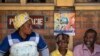 Patients waiting for prescriptions to be filled by the hospital pharmacy sit underneath a sign warning about the symptoms of Ebola, at Kibogora district hospital, near Lake Kivu and close to the border with Congo, in western Rwanda, Nov. 4, 2019.