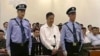 In this image taken from video, disgraced politician Bo Xilai, center, stands in the courtroom, flanked by police guards at Jinan Intermediate People's Court in eastern China's Shandong province, Aug. 22, 2013.