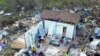 Two Haitian migrants sit as one stands amid the ruins of a home destroyed by Hurricane Dorian in Abaco, Bahamas, Sept. 28, 2019. 