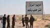 FILE - This photo released Sept 3, 2017 by the Syrian official news agency SANA, shows Syrian troops and pro-government gunmen standing next to a placard in Arabic which reads, "Deir el-Zour welcomes you," in the eastern city of Deir el-Zour, Syria. 